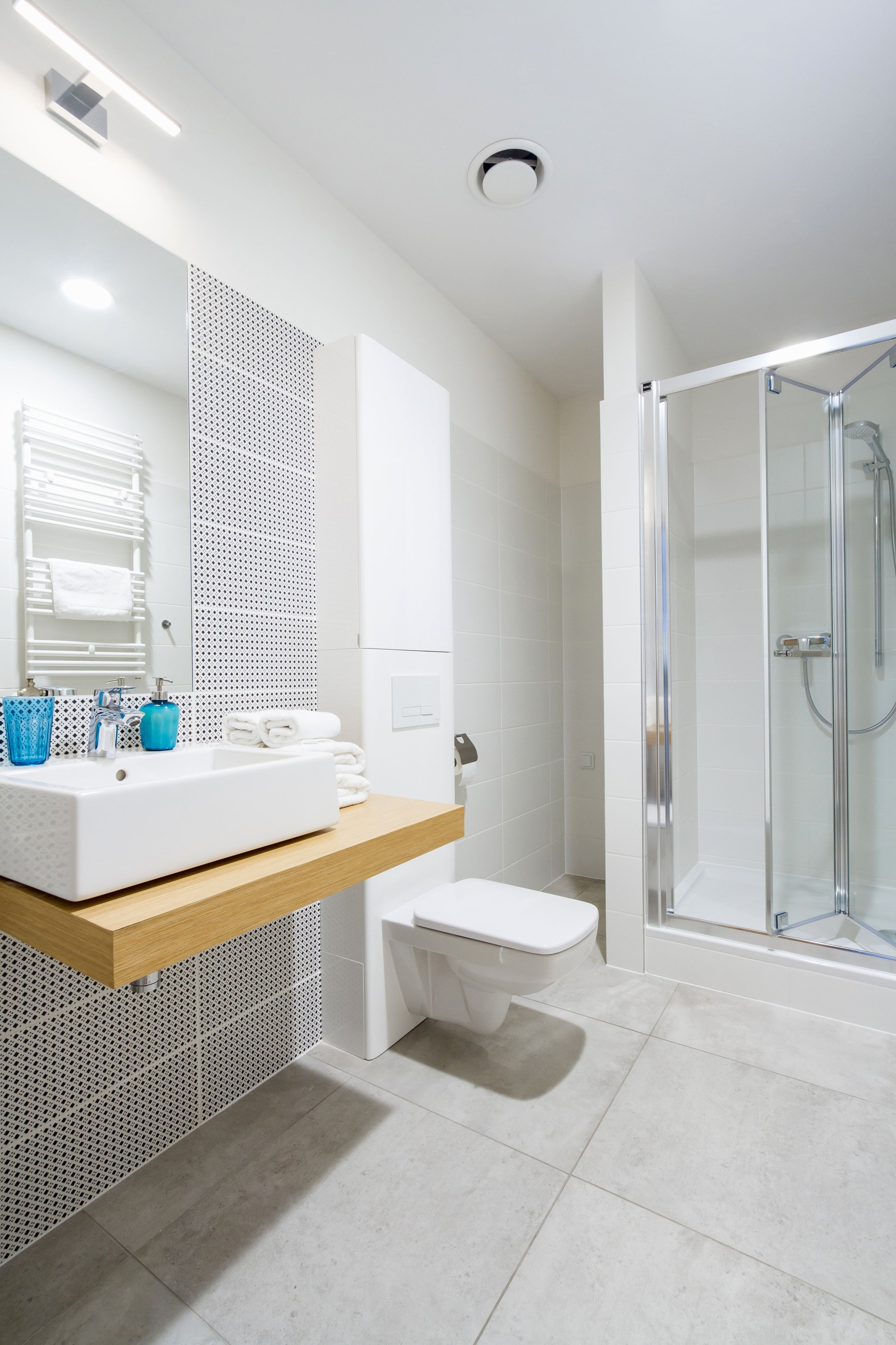 A modern bathroom with a white sink, blue cups, a glass shower enclosure, and a tiled floor.