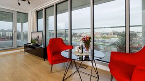 A modern living room with large windows, a glass table, and red chairs.