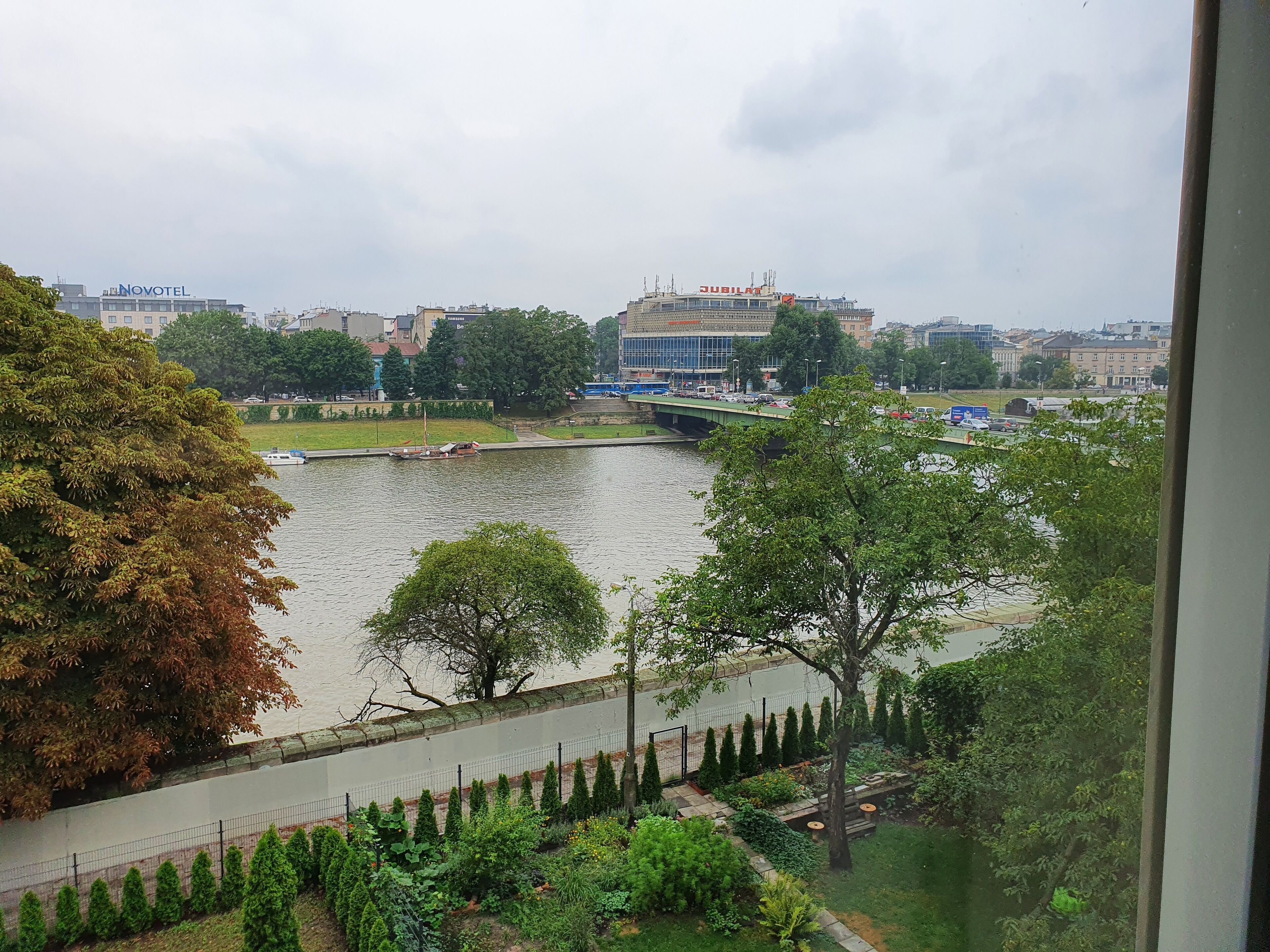 A view of a river with a bridge, trees, and buildings including a Novotel and a Jubilant hotel.