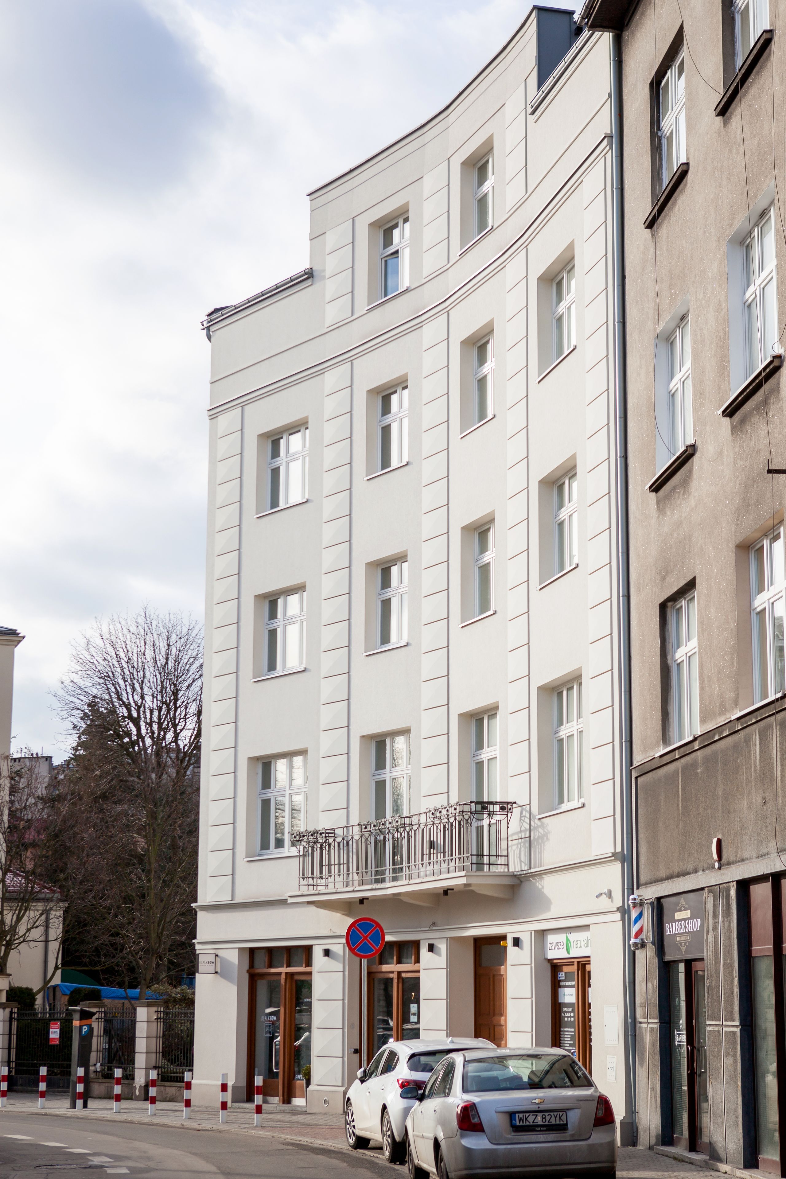 A multi-story building with a white facade, a visible entrance, and a barber shop sign.