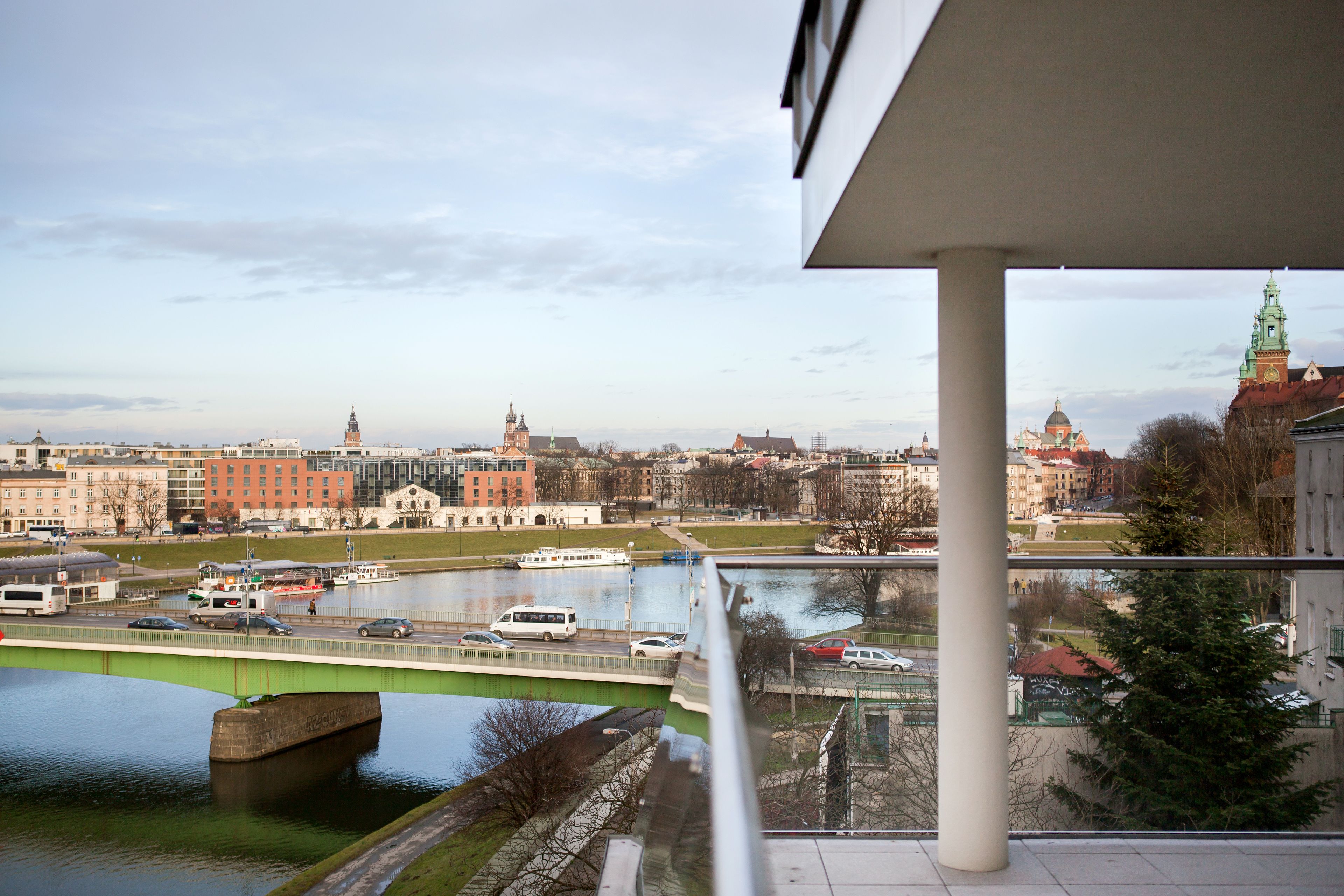 A view from a balcony overlooking a river with a bridge, buildings, and a clock tower.
