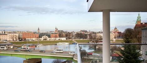A view from a balcony overlooking a river with a bridge, buildings, and a clock tower.