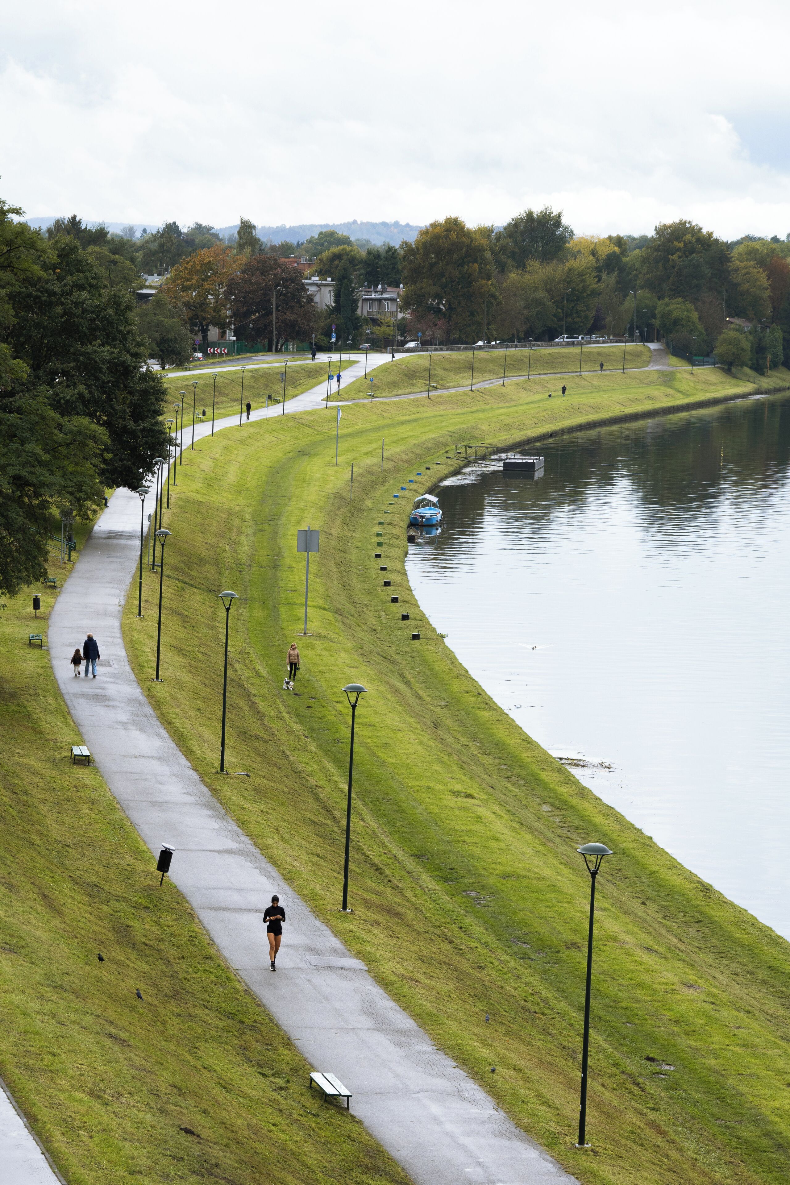 A park path alongside a lake with benches and lamp posts.