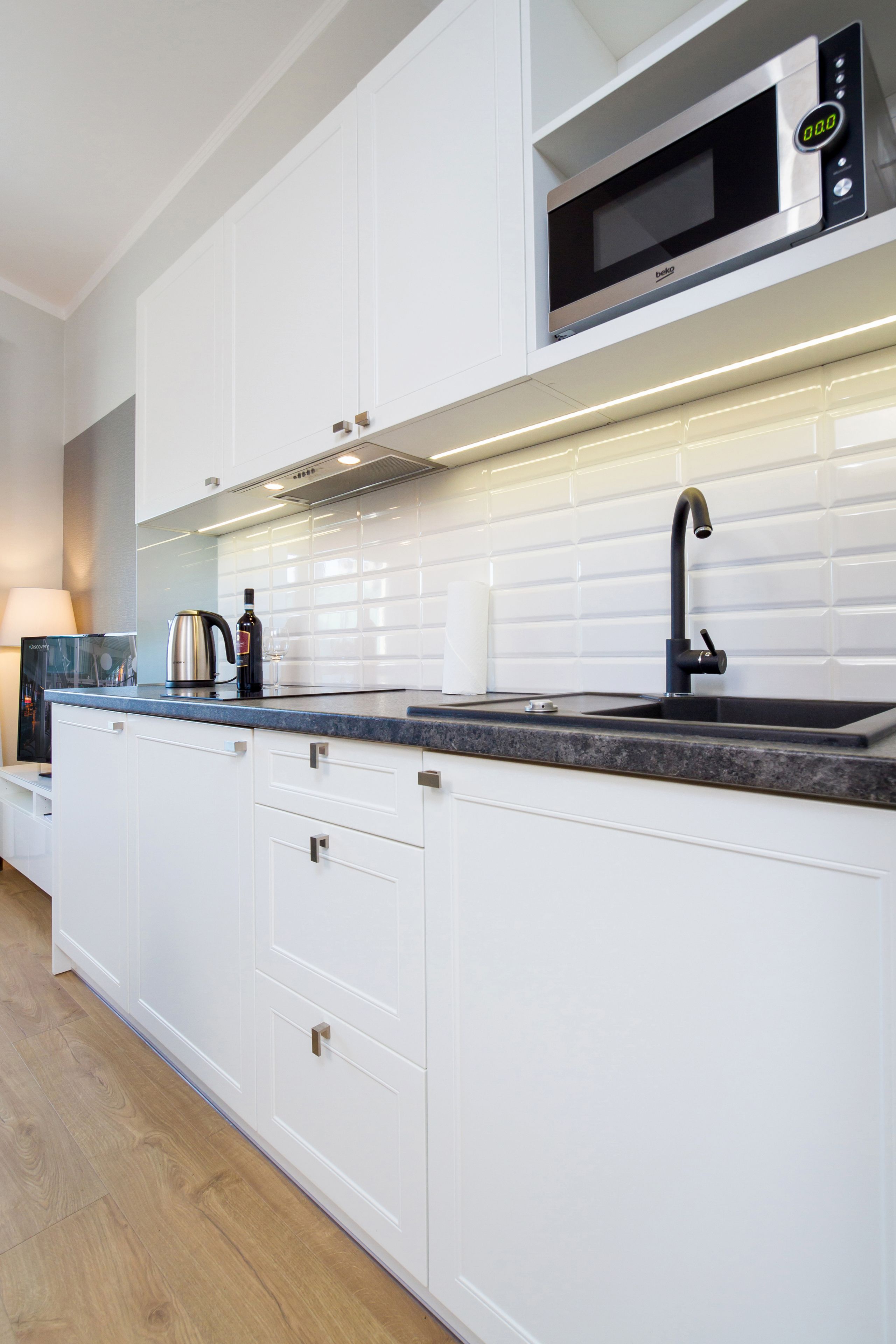 A modern kitchen with white cabinets, a black faucet, and a microwave above the sink.