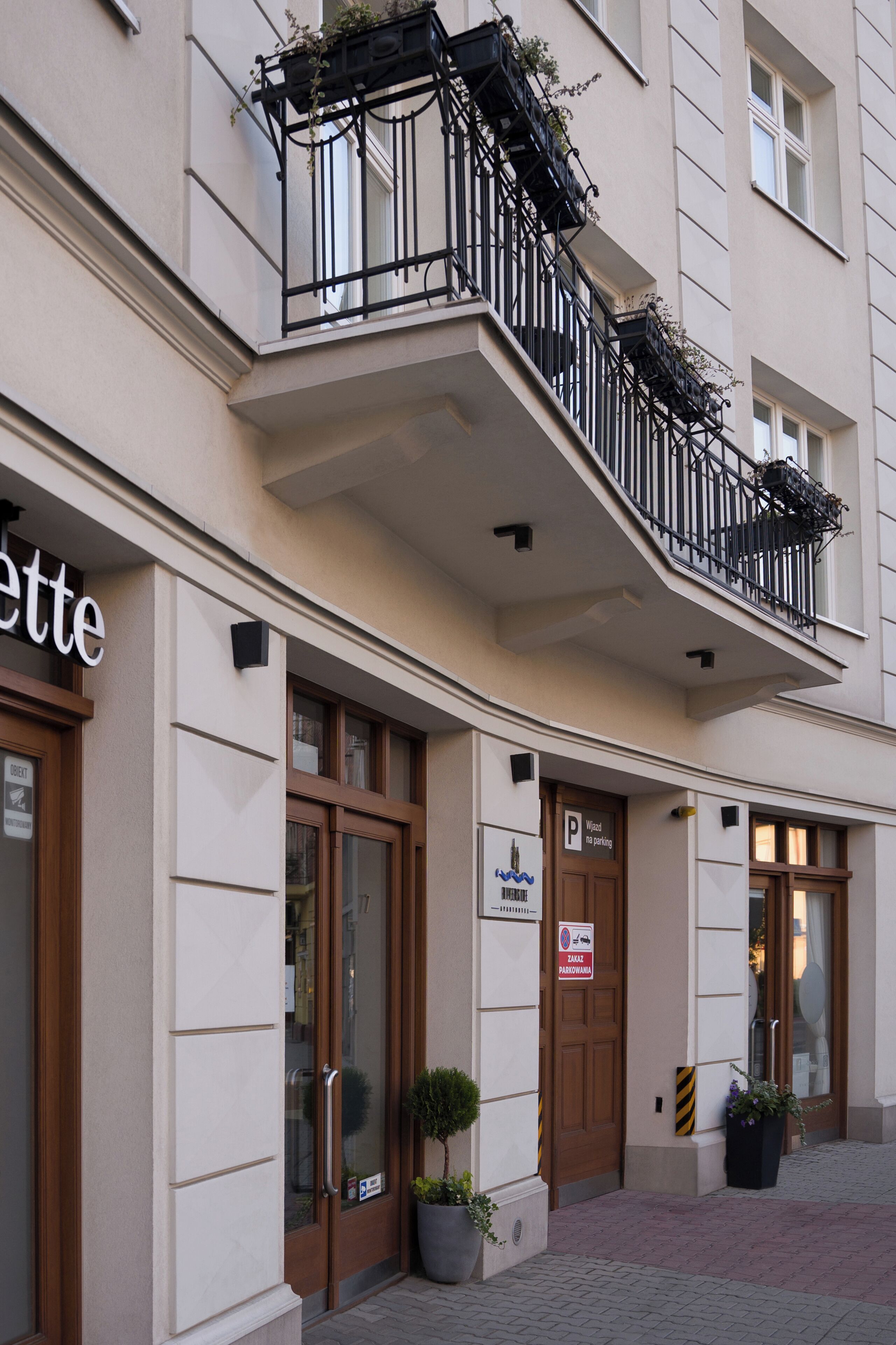 A hotel facade with a ground-floor entrance, a balcony with black railings, and a sign indicating parking availability.