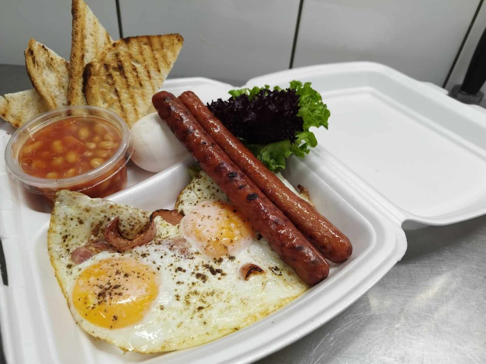 Un repas composé d’œufs, de saucisses, de pain grillé et d’une salade, le tout servi sur un plateau blanc.