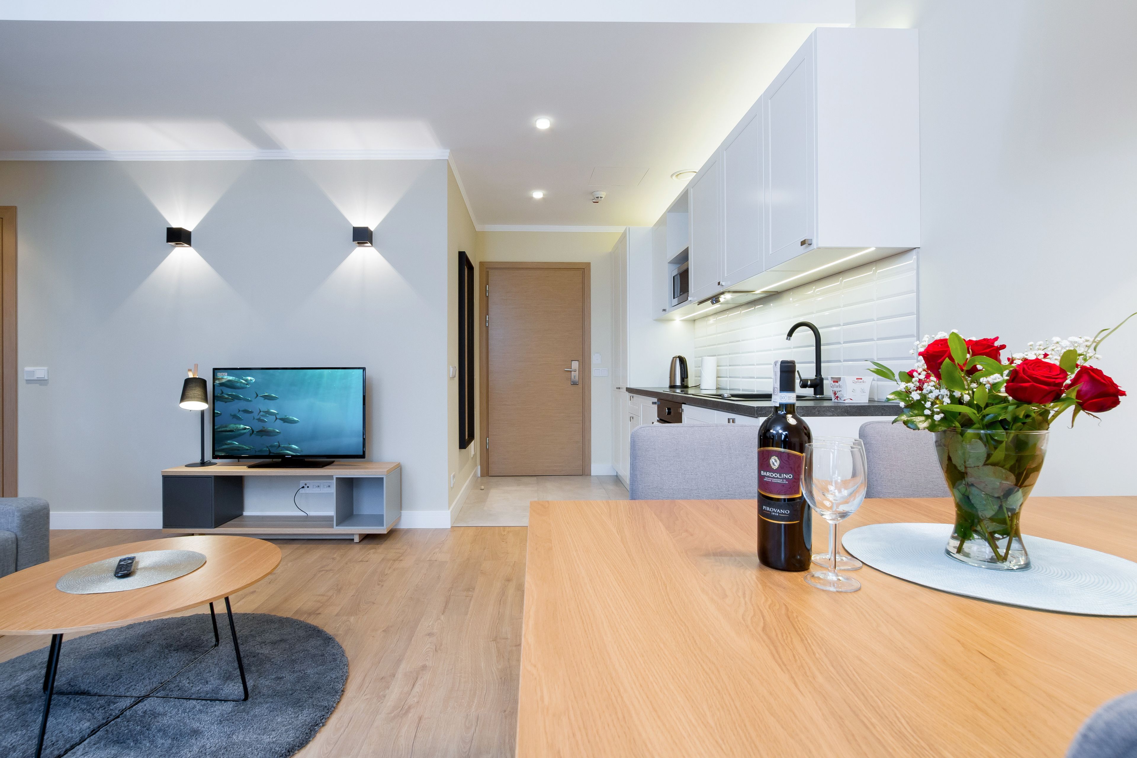 A modern living room with a TV, a dining table, and a kitchen area with a microwave.