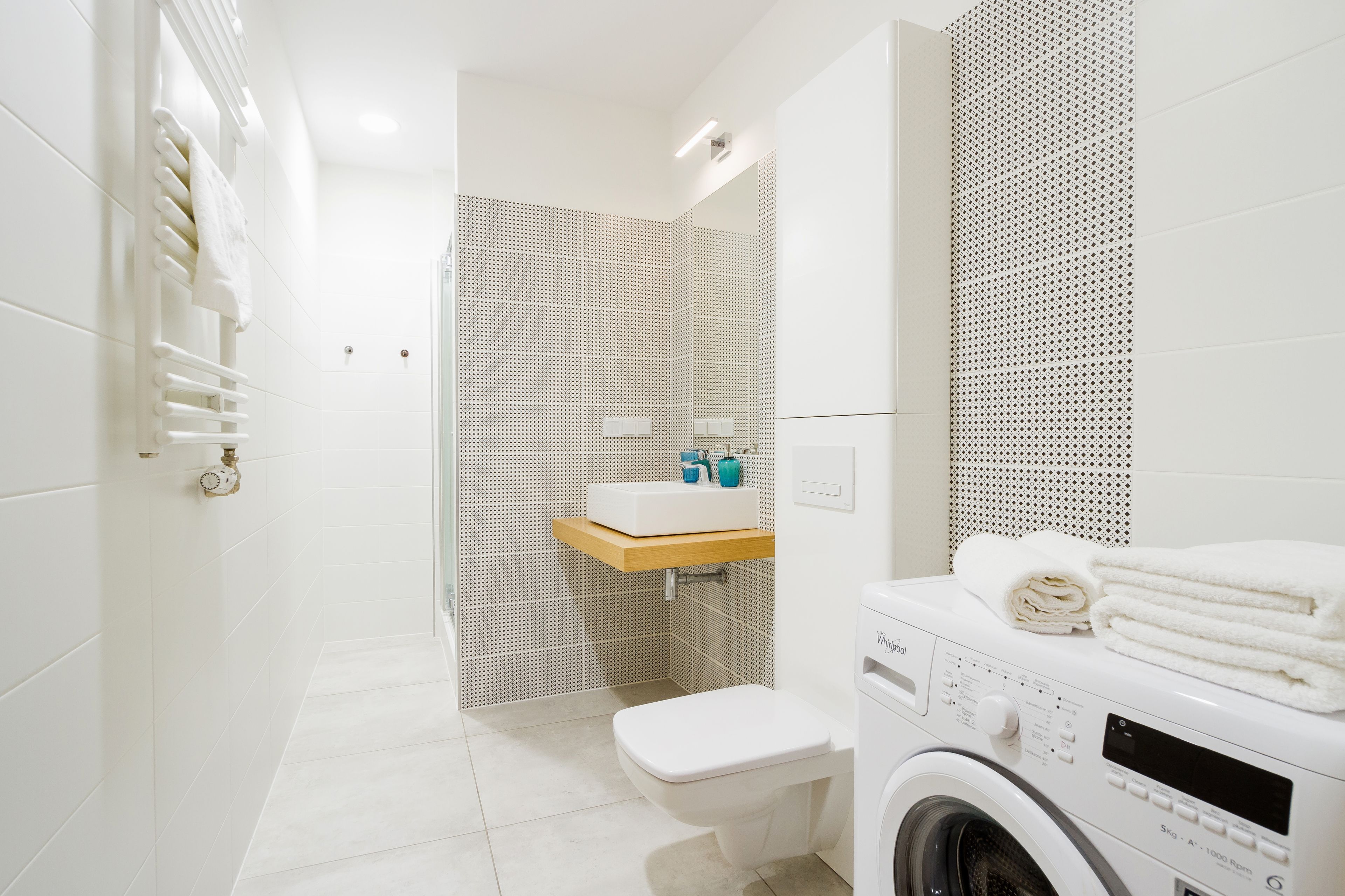 A compact, modern bathroom with a built-in washing machine, a toilet, and a sink with a wooden countertop.