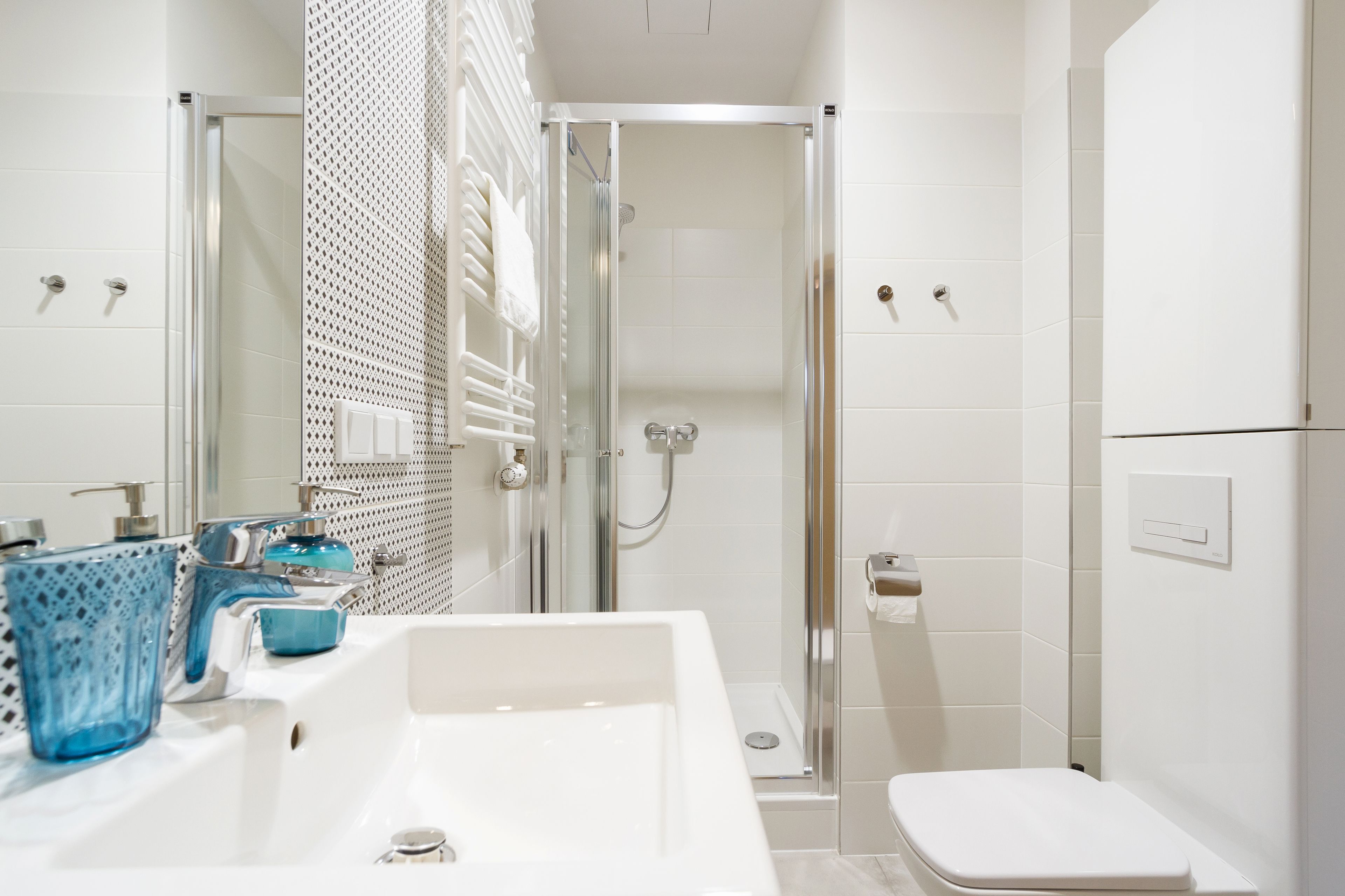 Een moderne badkamer met een witte wasbak, een blauwe glazen zeepdispenser en een douche met glazen wanden.