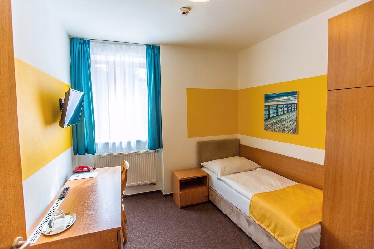 A compact hotel room with a bed, a desk, and a chair.