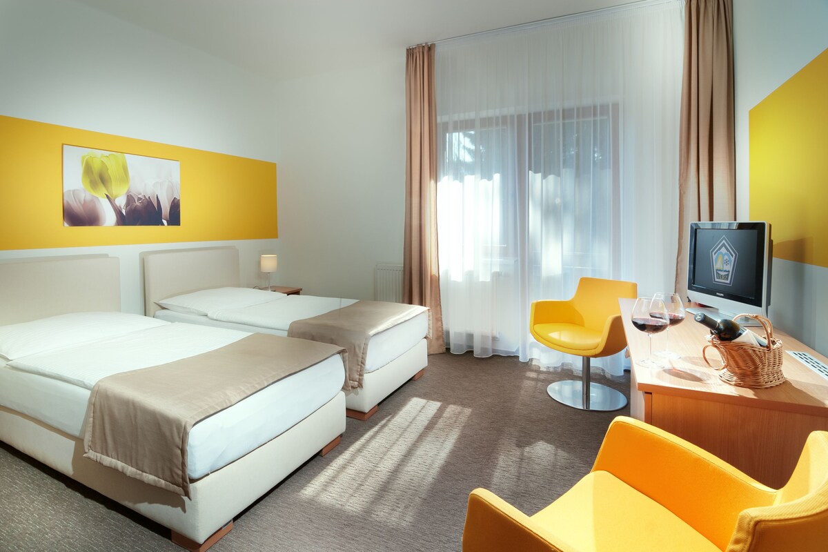 A hotel room with two beds, a desk with a computer, a chair, and a window with curtains.