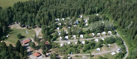 An aerial view of a campground with multiple RVs and cabins, surrounded by dense forest.