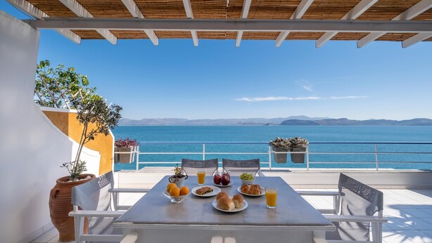 Mesa dispuesta con comida y bebidas en un balcón con vistas al mar.