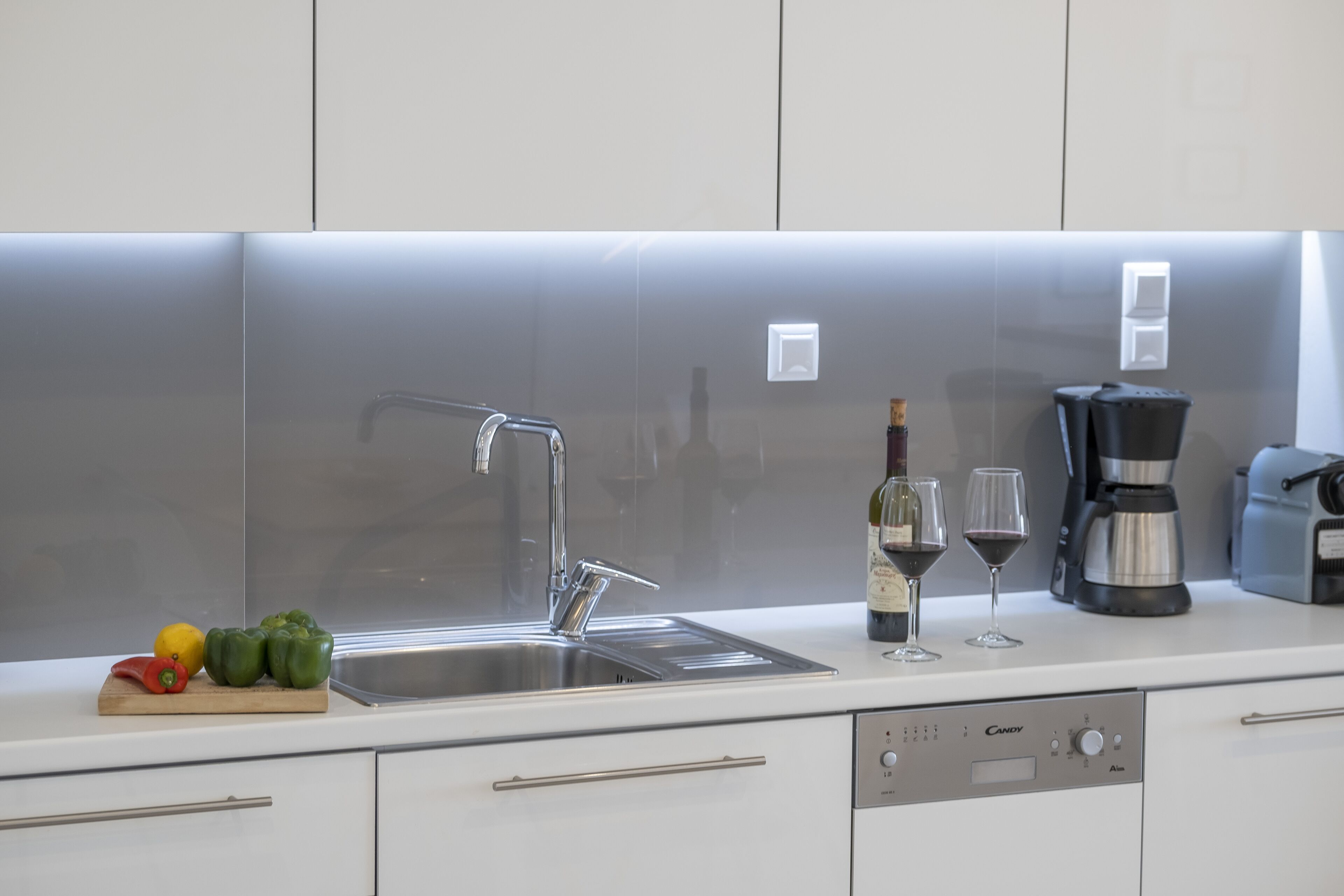 Une cuisine moderne avec un évier en acier inoxydable, une bouteille de vin, deux verres à vin et une machine à café.