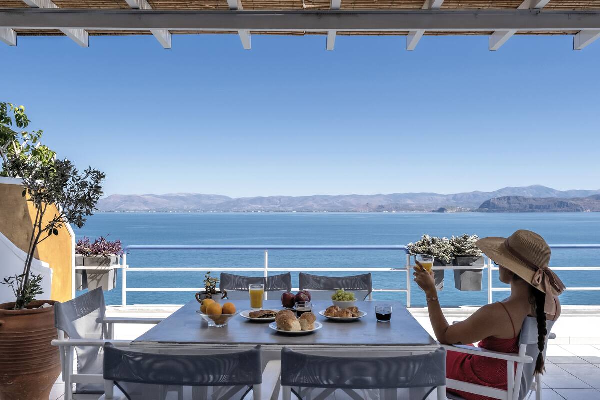 Una terraza con una mesa dispuesta para el desayuno, con vistas a un cuerpo de agua y montañas.