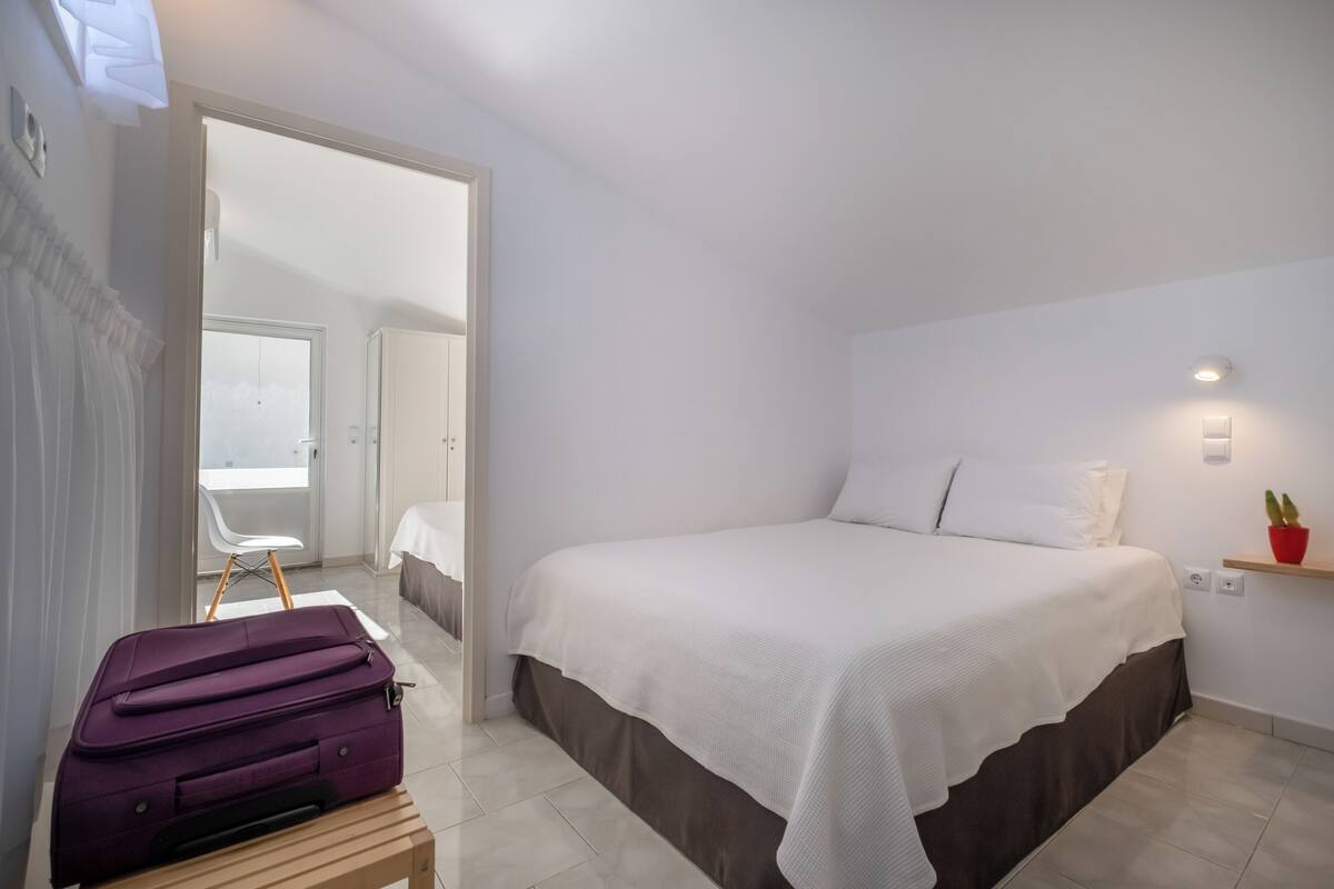 Un dormitorio con una cama, una maleta, una silla y una mesita.