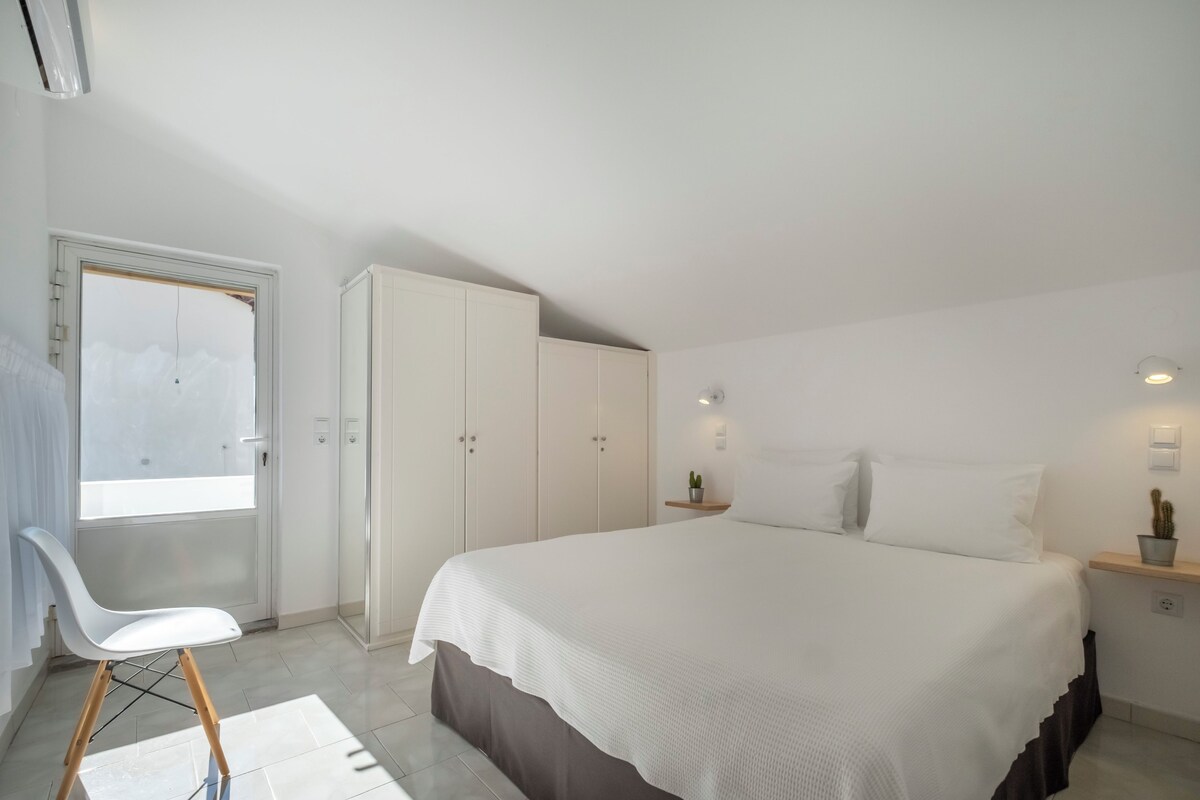 Un dormitorio con cama, una silla, un armario y ventana.