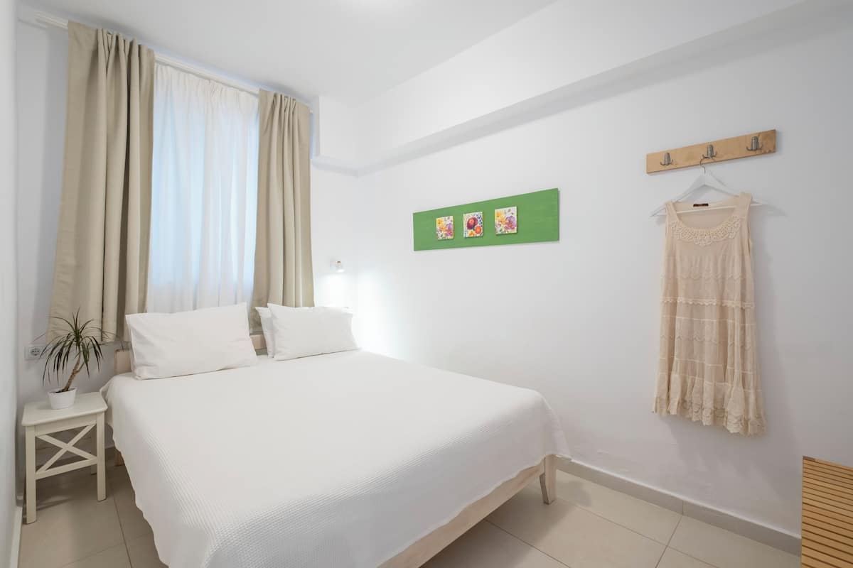 Un dormitorio con cama, mesita de noche, planta en maceta, perchero en la pared y una obra de arte verde.
