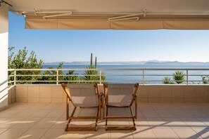 Un balcon avec deux chaises en bois, un auvent beige et une vue sur la mer et les montagnes.