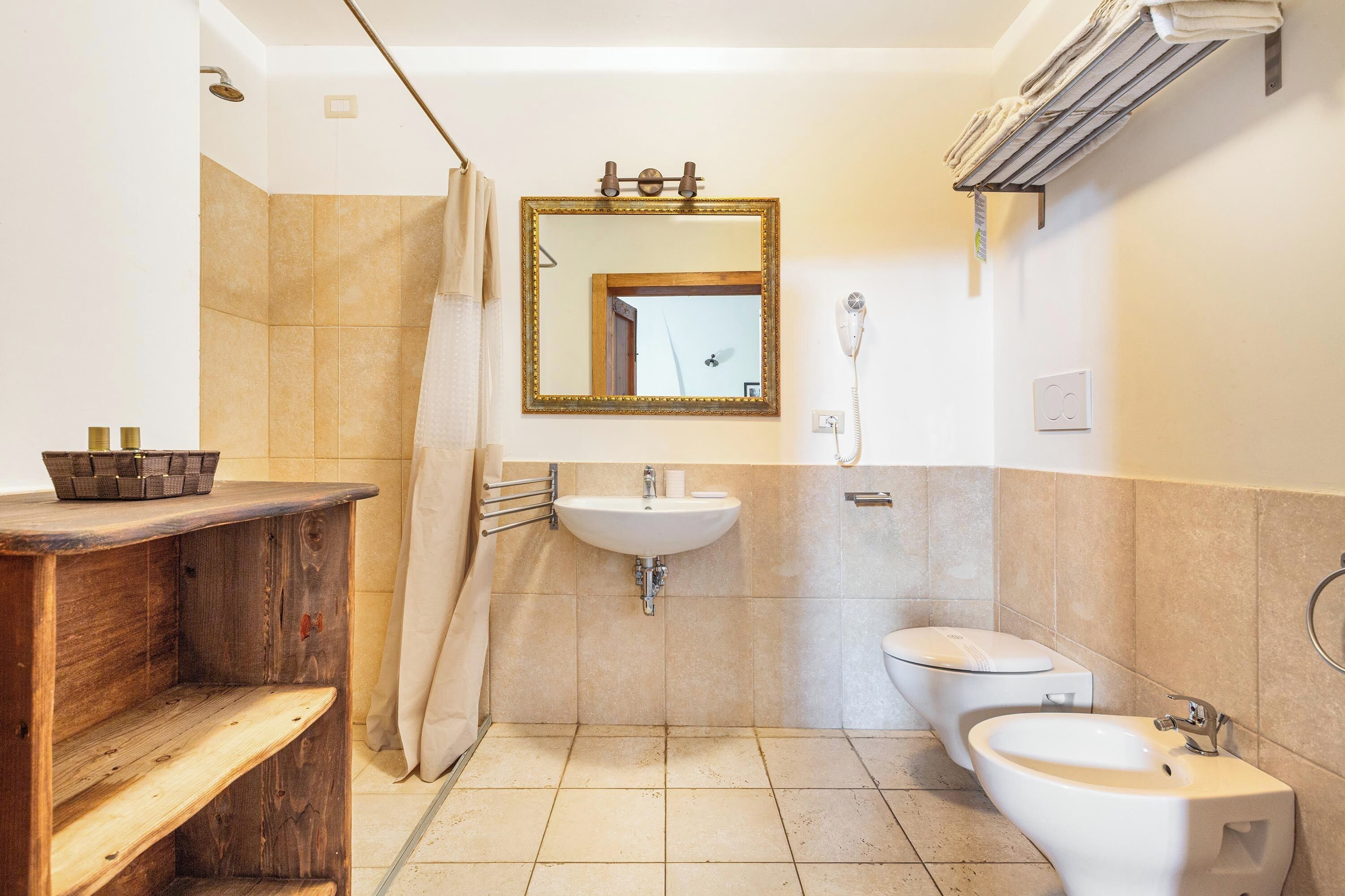 Un baño con tocador de madera, lavamanos, inodoro y ducha.