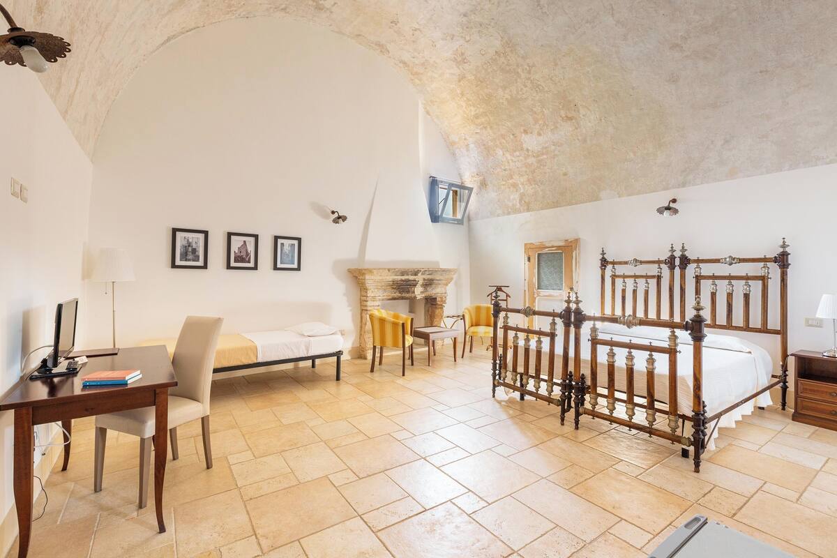 Ein Schlafzimmer mit einem großen Bett, einem Schreibtisch, einem Stuhl, einem Kamin und einer Steinwand.
