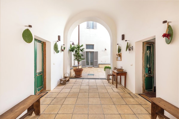 A corridor with a tiled floor, benches, a potted plant, and a door with a green frame.