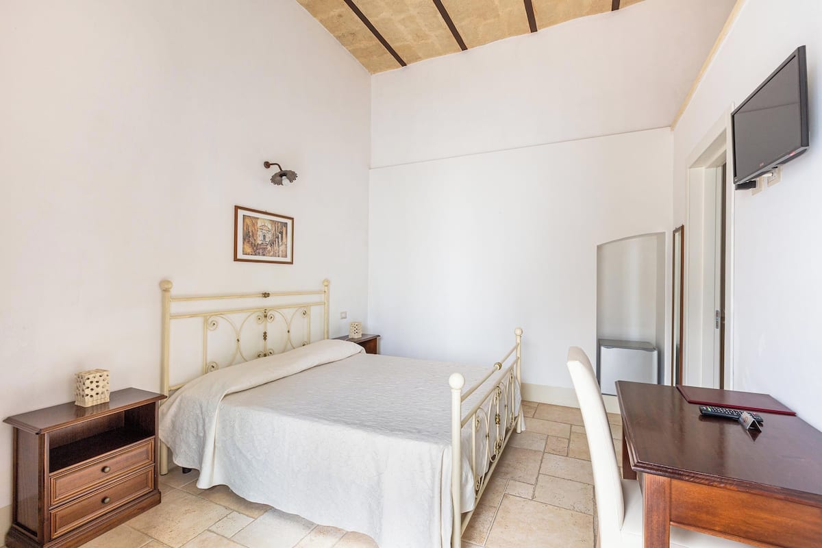 Ein Schlafzimmer mit Bett, Nachttisch und einem an der Wand befestigten Fernseher.