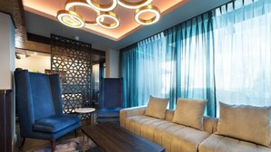 Una habitación de hotel moderna con sofá, sillones, una mesita de centro y un panel decorativo en la pared.
