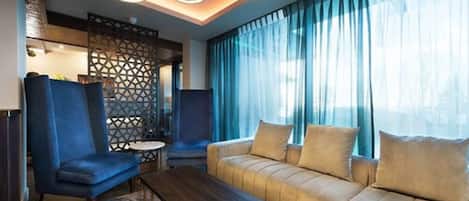 Una habitación de hotel moderna con sofá, sillones, una mesita de centro y un panel decorativo en la pared.