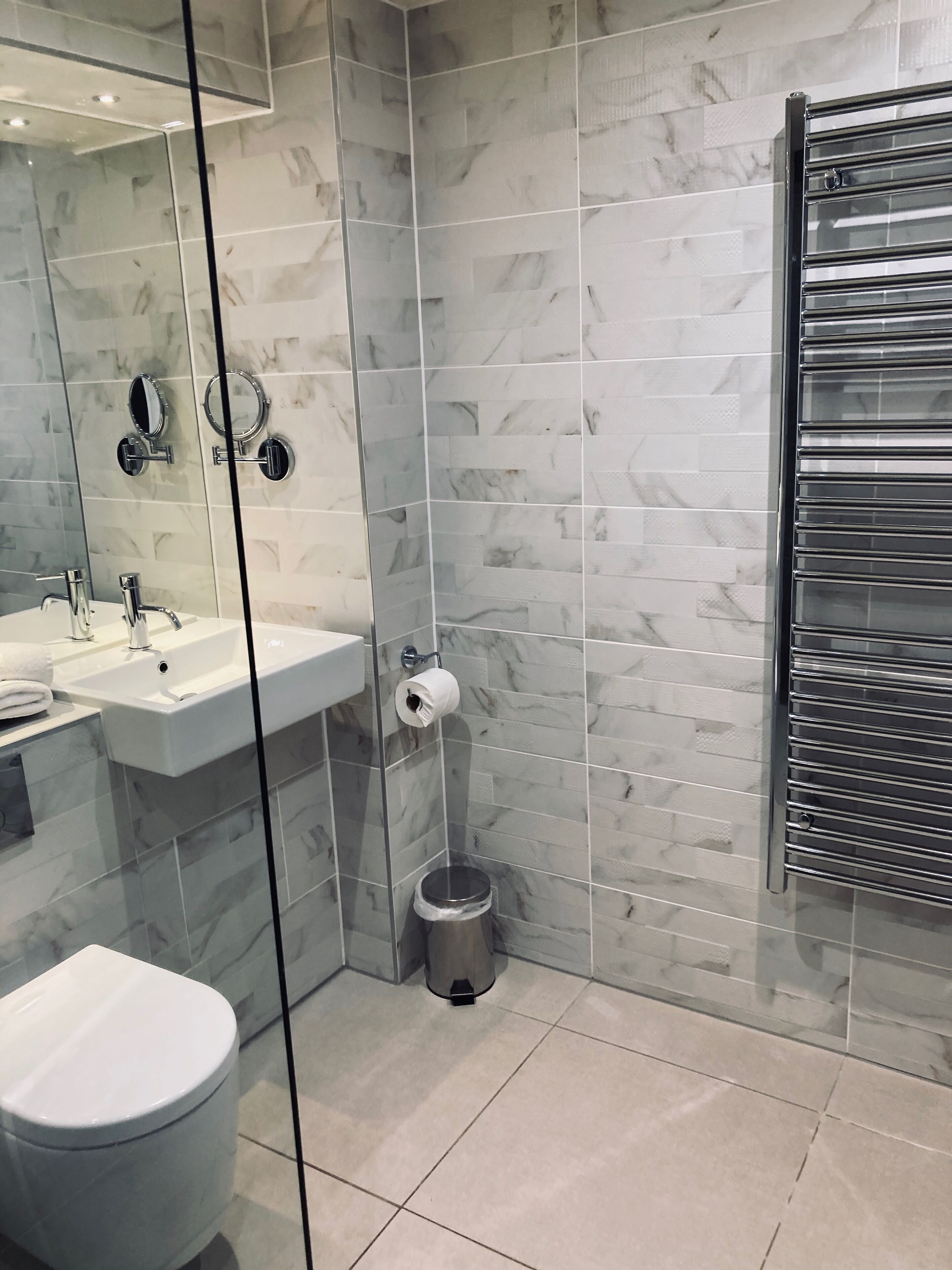 Une salle de bain moderne avec une cloison en verre, un lavabo blanc, des toilettes et un porte-serviettes.