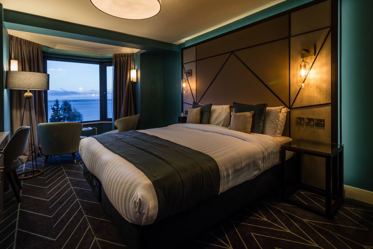 A modern hotel room with a large bed, a desk, and a view of the water.