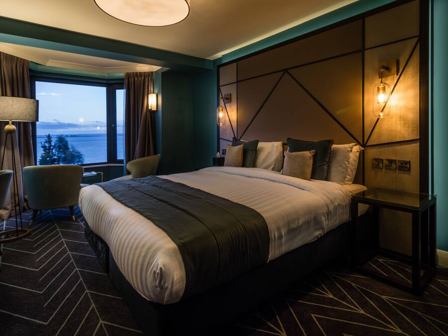 A modern hotel room with a large bed, a desk, and a view of the water.