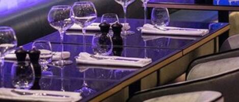 Un ambiente de restaurante con una larga mesa dispuesta para comer, incluyendo copas de vino, platos y cubiertos.