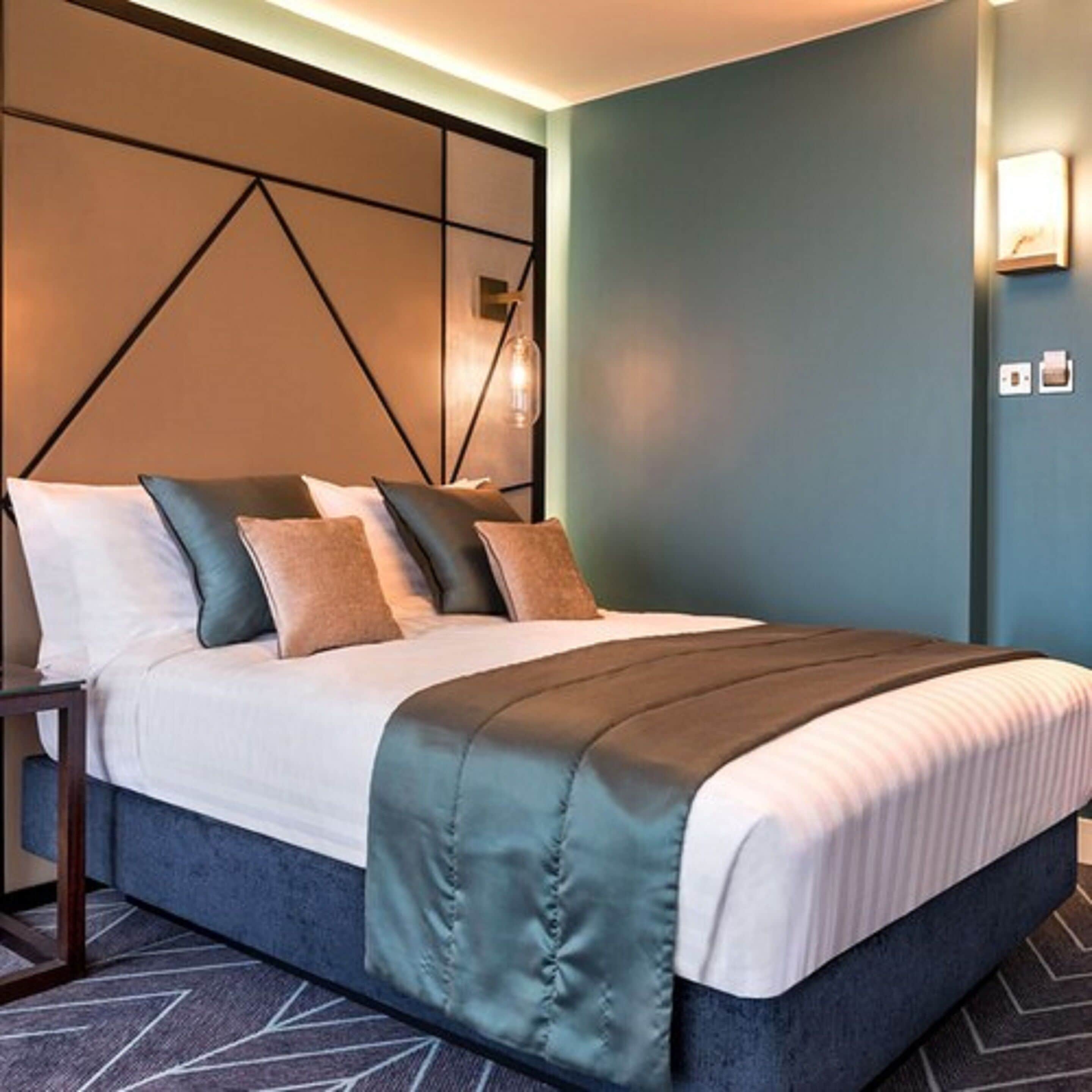 Ein Hotelzimmer mit einem Bett, einem Nachttisch, einer Wandlampe und einer Steckdose.