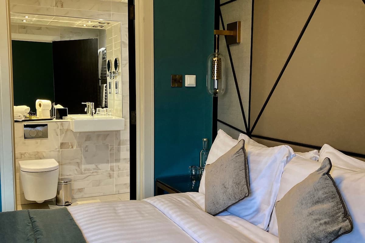 A modern hotel room with a large bed, a bathroom with a mirror, and a nightstand.