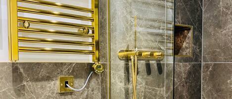 A modern bathroom with a glass-enclosed shower, gold fixtures, and marble tiles.