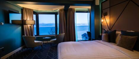 A hotel room with a large bed, a desk with a chair, and a view of the sea.