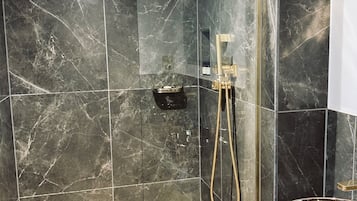 A modern bathroom with dark marble tiles, a shower with a gold fixture, and a hexagonal tile floor.