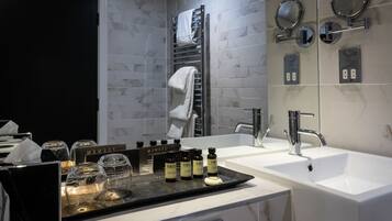 A modern bathroom with a white sink, a mirror, and a towel rack. There are also several bottles on the counter.