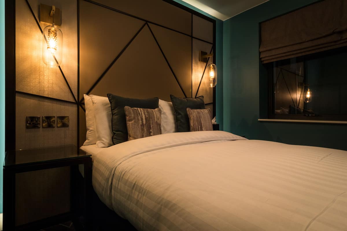 A neatly made bed with a headboard, a bedside table, and wall-mounted lights.