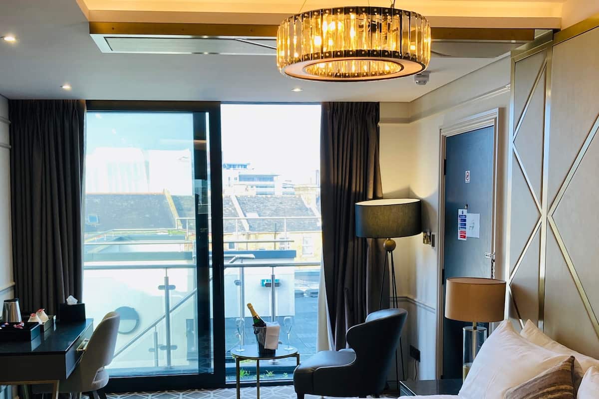 A hotel room with a large bed, a desk with a chair, a lamp, and a view of the city through the window.