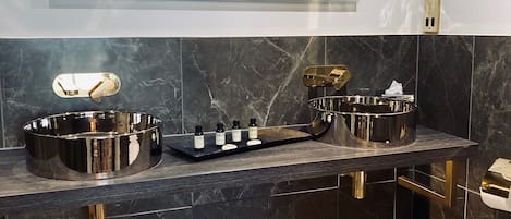 A modern bathroom with a dark marble countertop, gold fixtures, and a hexagonal tile floor.