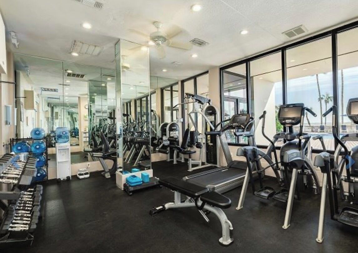 A gym with cardio machines, weight stations, and a mirror wall.