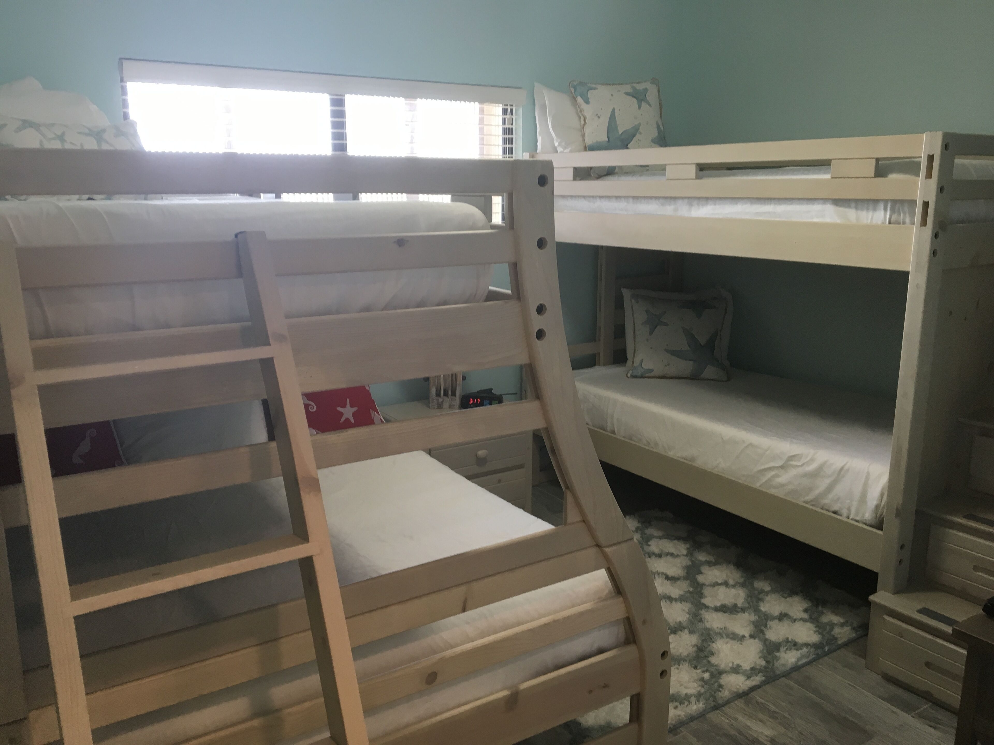 A bunk bed room with a window, a desk, and a patterned rug.
