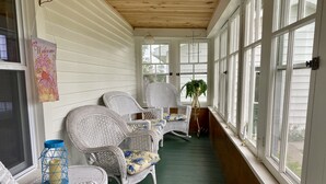 A covered porch with wicker chairs, a welcome sign, and large windows.