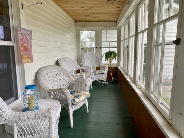 A covered porch with wicker chairs, a welcome sign, and large windows.