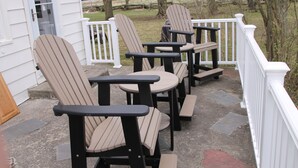 A porch with Adirondack chairs and a table, white railings, and a stone floor.