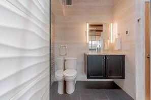Une salle de bain moderne avec deux toilettes, un meuble sombre et une cabine de douche en verre.