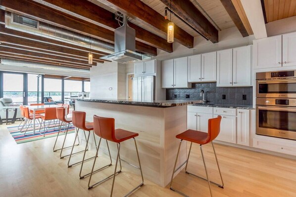 Une cuisine moderne avec des meubles blancs, des appareils en acier inoxydable et un coin bar doté de tabourets rouges.