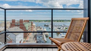 Un balcon avec une chaise en bois et une vue sur une marina, avec des bateaux et des bâtiments.